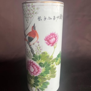 Peut inclure: Vase en céramique blanche avec un motif peint à la main représentant un oiseau rouge perché sur une branche, des pivoines roses et des feuilles vertes. Le vase a une bordure dorée et des caractères chinois.
