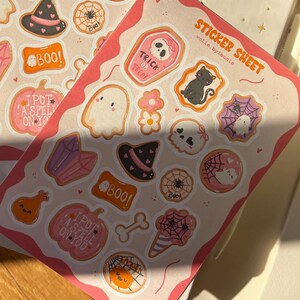 Könnte beinhalten: Zwei Bögen mit Halloween-Stickern mit verschiedenen Designs, darunter ein Hexenhut, Spinnennetze, Geister und Kürbisse. Die Aufkleber sind in Rosa, Orange, Schwarz und Weiß gehalten. Der Text auf den Aufklebern lautet "Boo!" und "Trick or Treat."