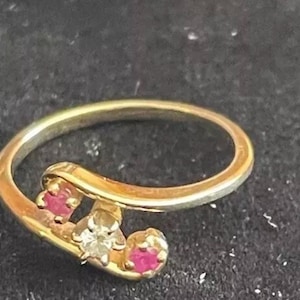 May include: A gold ring with three stones. Two of the stones are pink and one is clear.