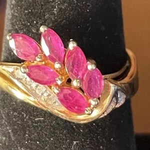 May include: A gold ring with a cluster of pink ruby stones set in a leaf design. The ring is accented with small diamonds.