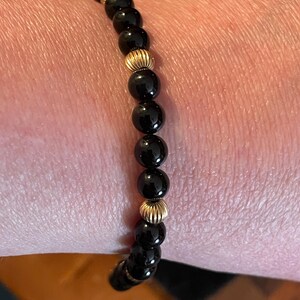 May include: A black and gold beaded bracelet with alternating black onyx and gold beads.