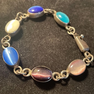 May include: Silver-toned bracelet featuring oval-shaped gemstones in various colors, including blue, turquoise, and purple. The bracelet has a chain link design and a clasp closure. A piece of jewelry.