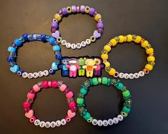 May include: Five colorful beaded bracelets with white letter beads spelling out names like "BLINKY" and "POKEY". Each bracelet features a unique color scheme, including blue, yellow, pink, green, and purple. A sticker with cartoon characters is in the center.