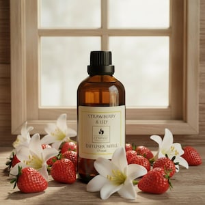 Könnte beinhalten: Eine braune Glasflasche mit Diffuser-Nachfüllflüssigkeit, schwarzem Verschluss und einem Etikett mit der Aufschrift Strawberry & Lily, 100ml. Die Flasche ist von frischen roten Erdbeeren und weißen Lilienblüten umgeben, was ein botanisches Bild ergibt.