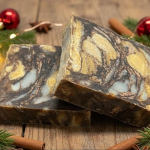 May include: Two rectangular bars of soap featuring a marbled pattern of dark brown, cream, and metallic gold swirls. The soap bars have a solid, dense texture with visible colour variations throughout the surface of each individual block.