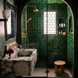 May include: A luxurious bathroom with emerald green tiled walls and a marble vanity. The shower features a gold showerhead and fixtures. A wooden stool sits in front of the shower. A decorative mirror and shelf are on the left.