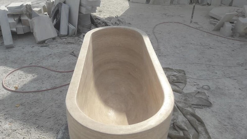 Puede incluir: Una gran ba&ntilde;era de forma ovalada, tallada en piedra de color claro. La ba&ntilde;era tiene bordes redondeados y un interior liso. La imagen est&aacute; tomada desde arriba, mostrando el interior de la ba&ntilde;era. El fondo incluye bloques de piedra y materiales de construcci&oacute;n.