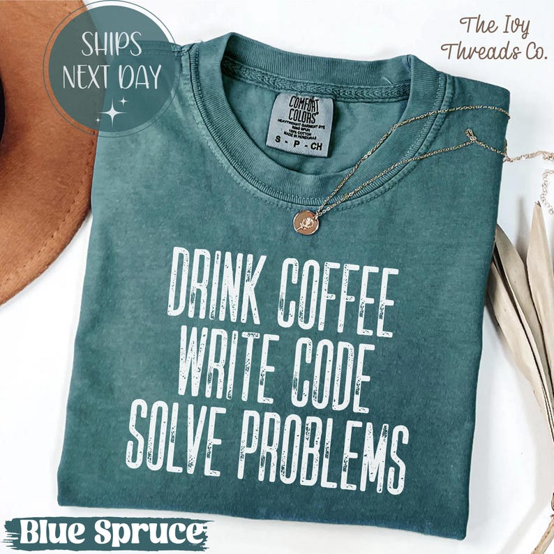Peut inclure: T-shirt bleu &eacute;pic&eacute;a avec le texte blanc "DRINK COFFEE WRITE CODE SOLVE PROBLEMS". Le t-shirt a un col rond et des manches courtes. Un collier en or avec un pendentif est drap&eacute; sur le t-shirt.