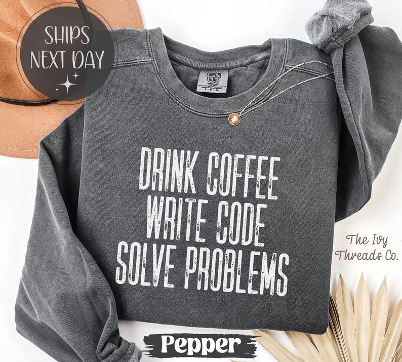 Peut inclure: Un sweat-shirt gris fonc&eacute; avec l'inscription blanche "DRINK COFFEE WRITE CODE SOLVE PROBLEMS". Le sweat-shirt a des manches longues et un col rond. Le mot "Pepper" est en bas de l'image.