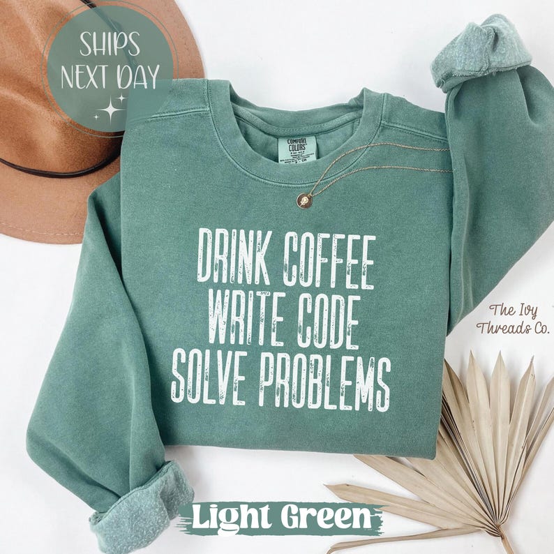 Peut inclure: Sweat-shirt vert clair avec le texte "DRINK COFFEE WRITE CODE SOLVE PROBLEMS" en blanc. Le sweat-shirt a un col rond et des manches longues avec des poignets roul&eacute;s. Un collier dor&eacute; est visible. Les mots "Light Green" sont en bas.