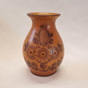 May include: A small, brown ceramic vase with a floral design. The vase has a rounded body and a narrow neck.