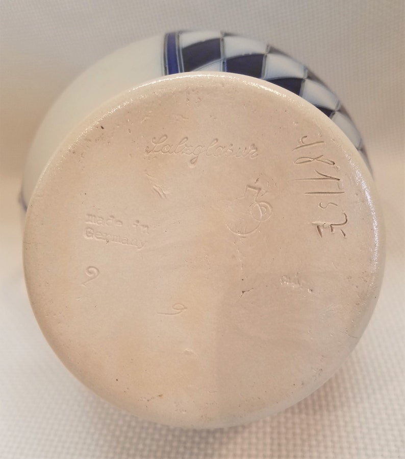 May include: White ceramic vase with a blue and white checkered pattern. The bottom of the vase is marked with the text "Salz glasur" and "Made in Germany".