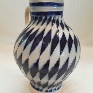 May include: A white ceramic pitcher with a blue and white diamond pattern. The pitcher has a handle and a wide mouth.