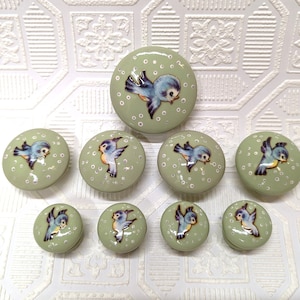 May include: Set of eight green ceramic knobs with bluebird illustrations. The knobs have a white background with small white dots. The birds are in various flying positions.