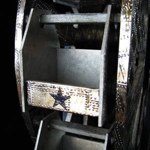 May include: A silver metal Ferris wheel with a blue star design. The wheel has multiple compartments that can be used for storage.