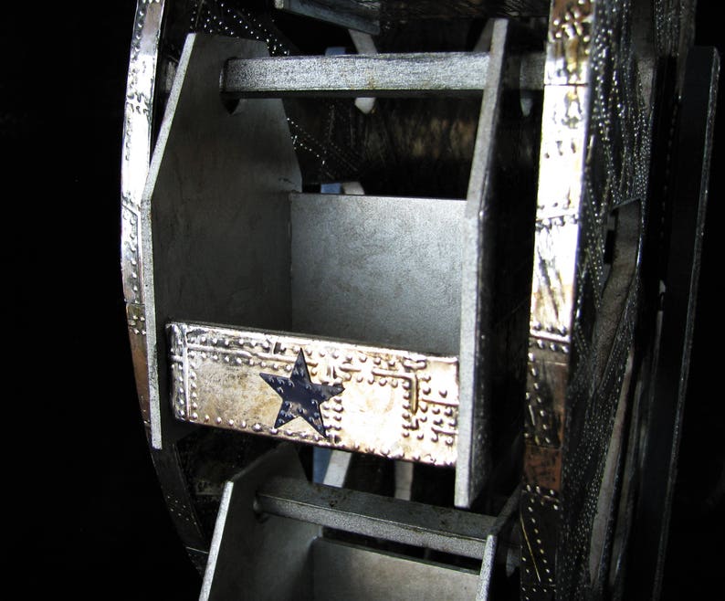 May include: A silver metal Ferris wheel with a blue star design. The wheel has multiple compartments that can be used for storage.