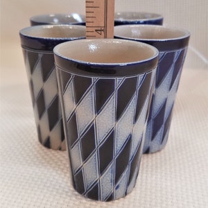 May include: Set of four blue and white ceramic shot glasses with a diamond pattern. The glasses are stacked on top of each other.
