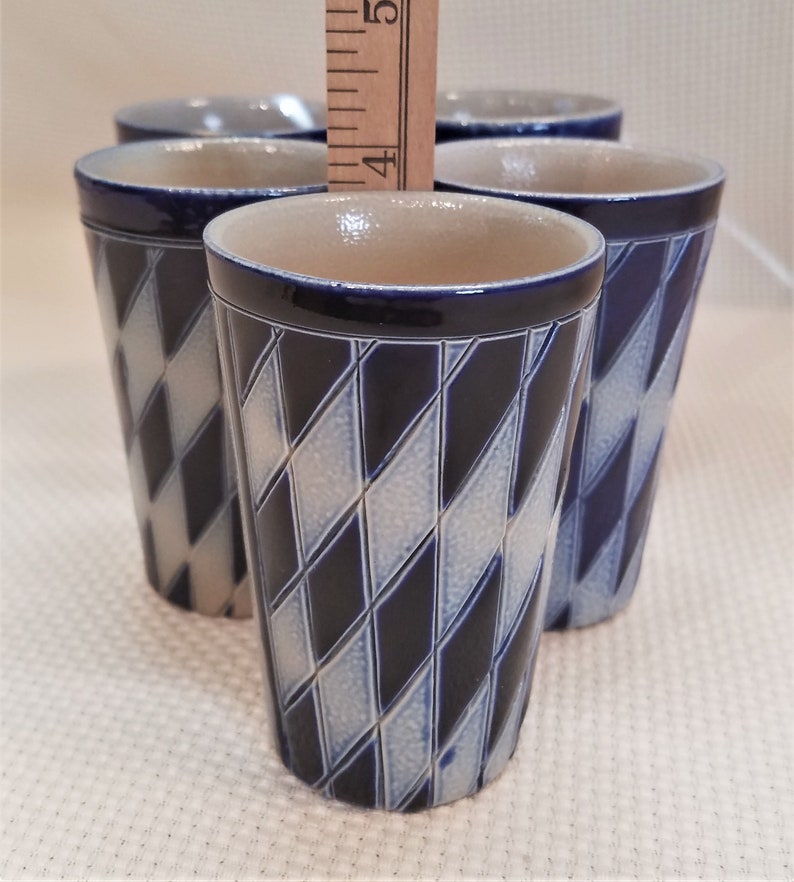 May include: Set of four blue and white ceramic shot glasses with a diamond pattern. The glasses are stacked on top of each other.