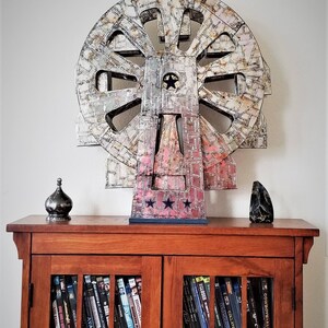 May include: A large, multi-coloured, circular sculpture with a star in the centre, sitting on a wooden cabinet with glass doors. The cabinet is filled with DVDs.