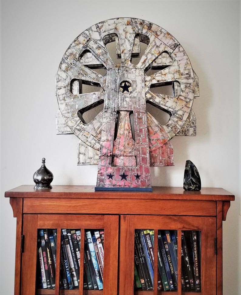 May include: A large, multi-coloured, circular sculpture with a star in the centre, sitting on a wooden cabinet with glass doors. The cabinet is filled with DVDs.