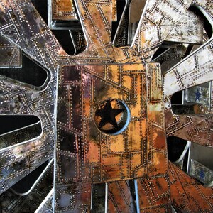 May include: A close-up of a metal structure with a star-shaped design in the centre. The structure is made of multiple panels, each with a different pattern of rivets and metalwork. The panels are arranged in a radial pattern, creating a sense of depth and complexity.