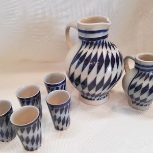 May include: A set of six ceramic cups and two ceramic pitchers with a blue and white diamond pattern. The cups are small and the pitchers are tall and round.