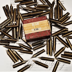 May include: A red box with gold lettering that reads "No. 170 JOSEPH GILLOTT'S" surrounded by a large quantity of gold-colored nibs for fountain pens.