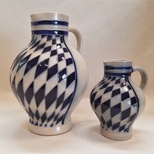 May include: Two ceramic pitchers with a blue and white diamond pattern. The larger pitcher has a handle and a wider base. The smaller pitcher is more compact and has a smaller handle.
