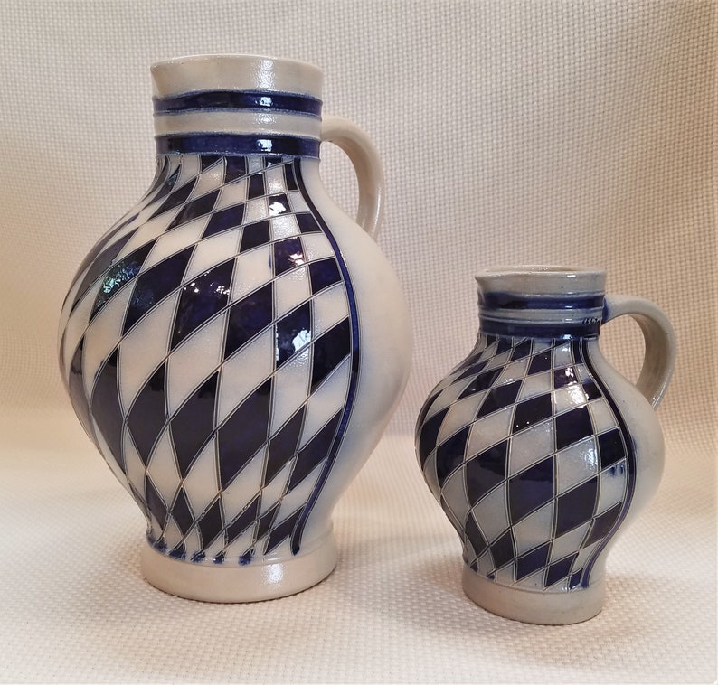 May include: Two ceramic pitchers with a blue and white diamond pattern. The larger pitcher has a handle and a wider base. The smaller pitcher is more compact and has a smaller handle.