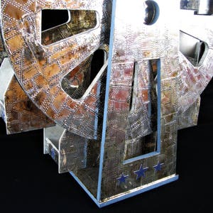 May include: A silver and copper-toned metal sculpture of a Ferris wheel with a textured surface. The sculpture has a base with three stars.