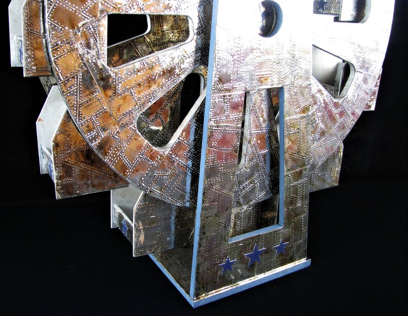 May include: A silver and copper-toned metal sculpture of a Ferris wheel with a textured surface. The sculpture has a base with three stars.