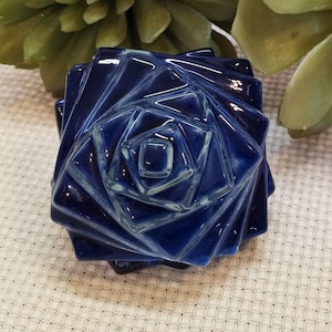 May include: A dark blue ceramic rose shaped trinket box. The box is made of glazed ceramic and has a geometric design.