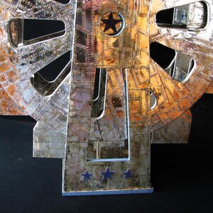 May include: A silver and copper-toned metal sculpture of a gear with a star in the centre. The sculpture is on a black background.