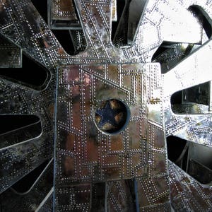 May include: A close-up of a silver metal structure with a circular pattern and a central hole. The structure is made of multiple layers of metal, each with a different pattern. The metal is shiny and reflective, and the structure has a complex and intricate design.