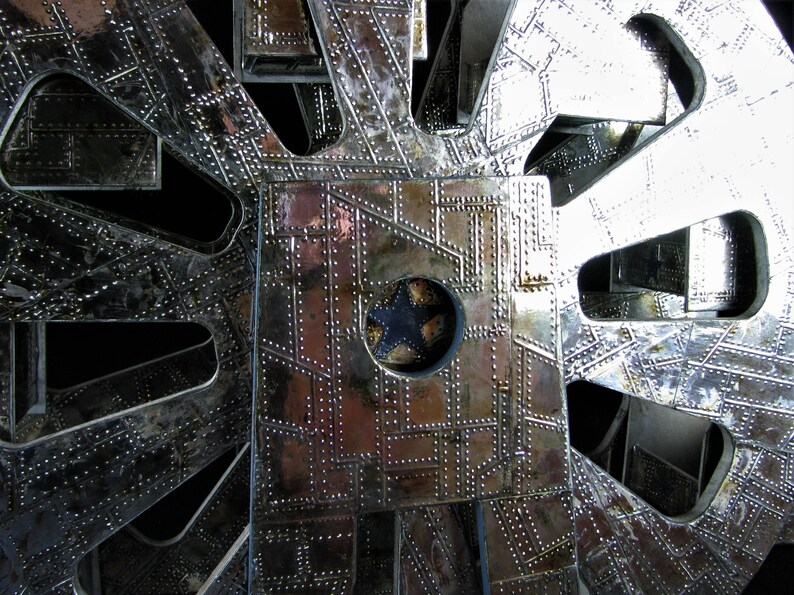 May include: A close-up of a silver metal structure with a circular pattern and a central hole. The structure is made of multiple layers of metal, each with a different pattern. The metal is shiny and reflective, and the structure has a complex and intricate design.