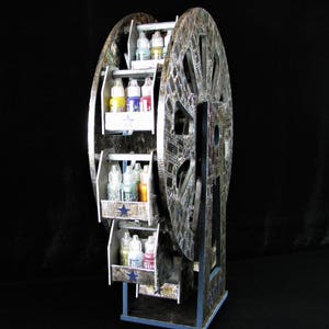May include: A silver and black Ferris wheel-shaped storage rack with multiple shelves for holding bottles of paint. The shelves are decorated with blue stars and the wheel is decorated with a silver and black pattern.