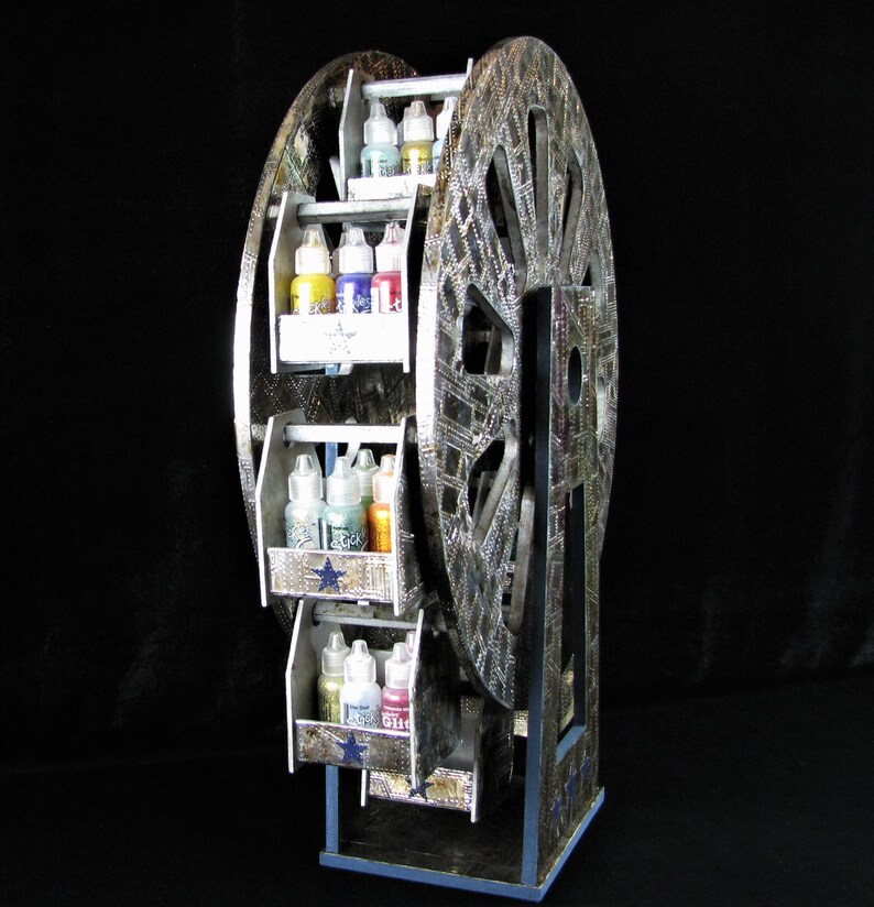 May include: A silver and black Ferris wheel-shaped storage rack with multiple shelves for holding bottles of paint. The shelves are decorated with blue stars and the wheel is decorated with a silver and black pattern.