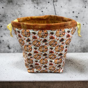 May include: A white drawstring bag with a brown and orange floral pattern. The bag has yellow drawstrings.