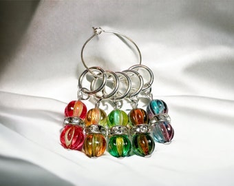May include: A set of six colorful glass bead stitch markers with silver rings and a silver hoop. The beads are in shades of red, orange, yellow, green, blue, and purple.