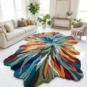 Könnte beinhalten: Ein farbenfroher, abstrakter Teppich mit einer einzigartigen, organischen Form. Der Teppich zeigt eine lebendige Palette aus Blau-, Grün-, Orange- und Gelbtönen und bildet einen auffälligen Blickfang. Das Design des Teppichs ähnelt einer stilisierten Blume oder einem Blatt und verleiht dem Raum einen Hauch von Kunst.