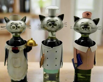 May include: Three metal cat bottle holders, each dressed in a different profession. One is a chef wearing a white chef's hat and a white apron, another is a maid wearing a white apron and a black bow tie, and the third is a nurse wearing a pink uniform and a white nurse's hat.