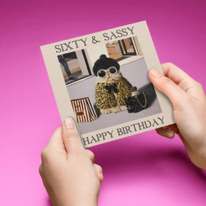 May include: A birthday card featuring a cat wearing sunglasses and a leopard print coat, holding a purse. The card says "Sixty & Sassy" and "Happy Birthday".