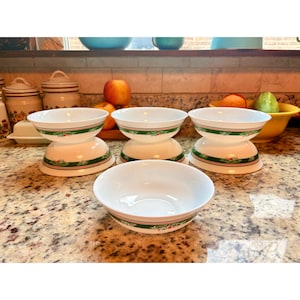 May include: A collection of white ceramic bowls with a green and floral design. The bowls are stacked and arranged on a speckled countertop, showcasing a vintage aesthetic. The bowls are ideal for serving soups, salads, or desserts.