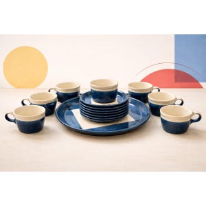 May include: A ceramic dinnerware set featuring a large serving plate, small plates, and cups. The set has a navy blue exterior with a cream-colored interior. The serving plate has a white square design in the center. The cups have handles.