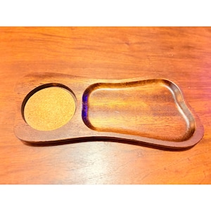 May include: A wooden tray with a circular coaster and a small, irregularly shaped compartment. The tray is made of dark brown wood with a smooth, glossy finish. The coaster is made of a light brown cork material.