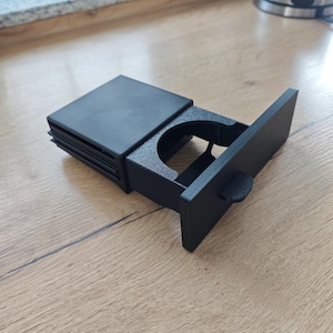 May include: Black plastic cup holder with a sliding lid. The cup holder is designed to fit in a car's centre console.