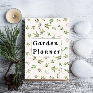 May include: A white spiral bound notebook with a green and white floral pattern. The notebook has the text "Garden Planner" printed on the front.