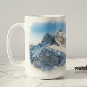 Puede incluir: Taza de cerámica blanca con un diseño de paisaje montañoso, que muestra picos nevados y un cielo azul. La taza tiene un asa grande y es adecuada para bebidas frías o calientes. La taza mide aproximadamente 13 cm de alto.
