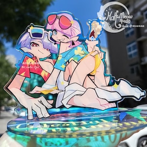 Peut inclure: Un présentoir en acrylique transparent avec une illustration colorée de style anime de deux personnages en maillot de bain. L'un porte des lunettes de soleil et une chemise bleue avec des étoiles jaunes. L'autre porte des lunettes de soleil et une chemise rouge.
