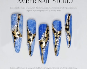 May include: Five long, blue and gold nail tips with rhinestones. The nails have a denim-like texture and a leopard print design.